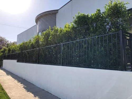 Modern building with a curved facade, bordered by a tall hedge and black metal fence. The scene conveys a sense of privacy and contemporary style.